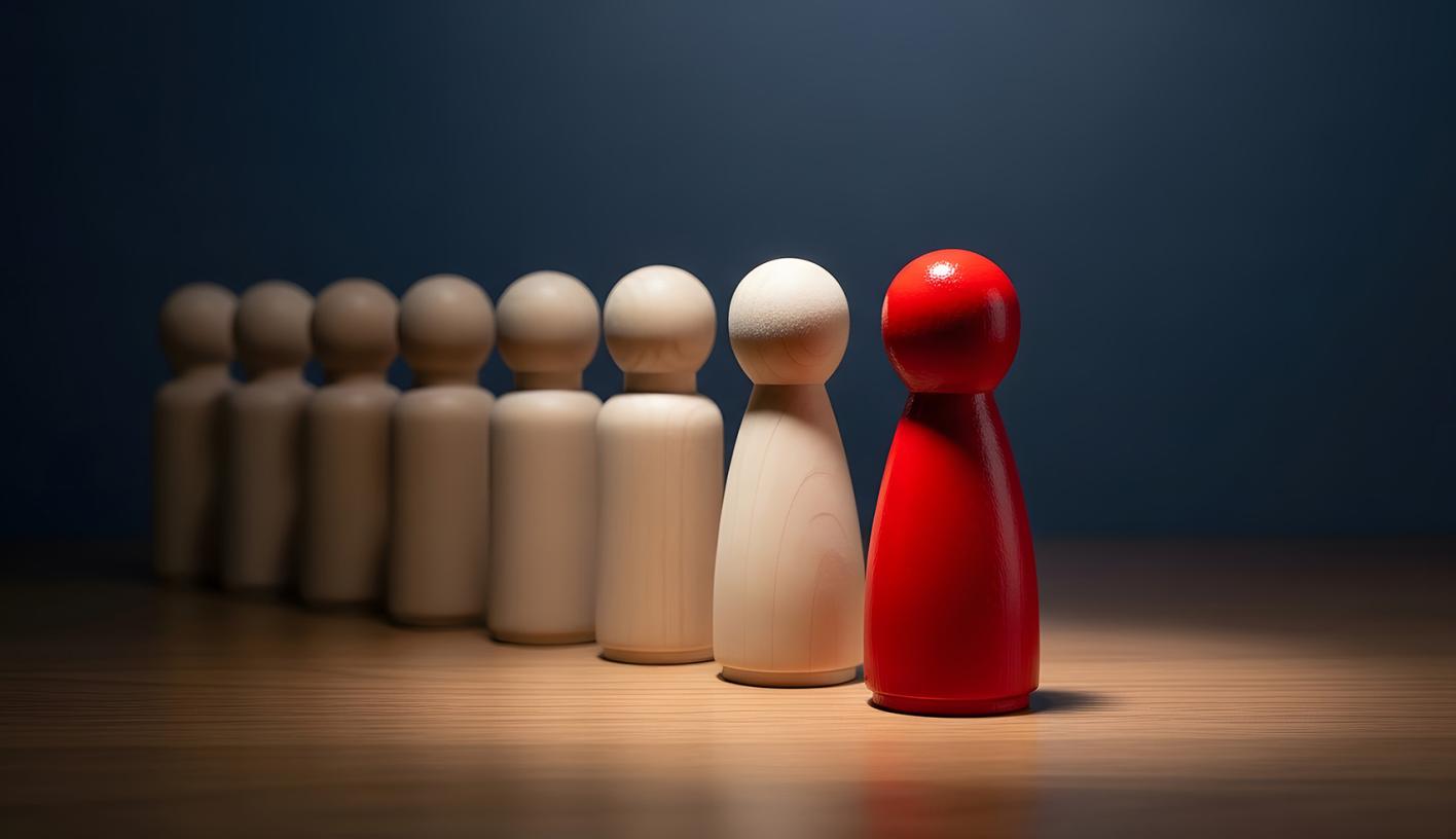 A red simplifed carving of a person leads a line of unpainted figures.