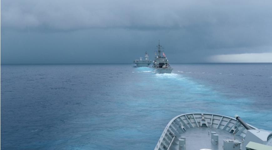 Modern Military Ships at sea headed towards a storm on the horizon.